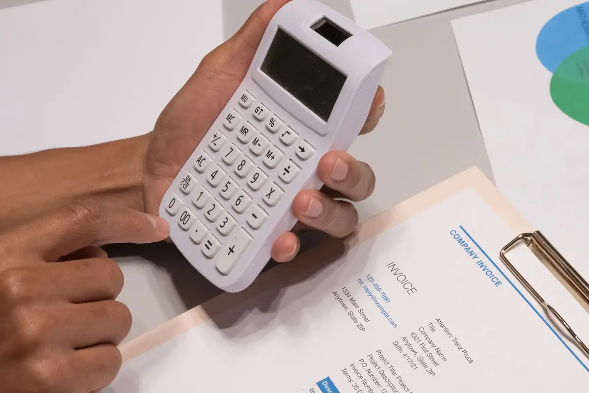 Hands using a calculator next to a company invoice