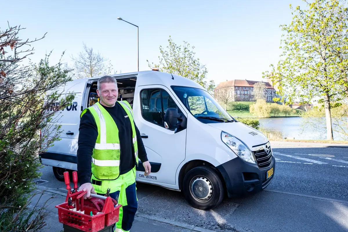 A smiling worker in a reflective vest standing beside a service van with his tools