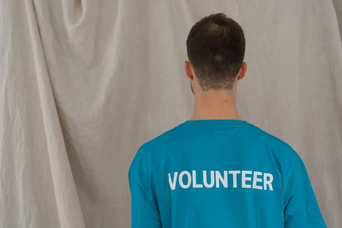 A volunteer photographed from behind wearing a shirt with VOLUNTEER printed across the back