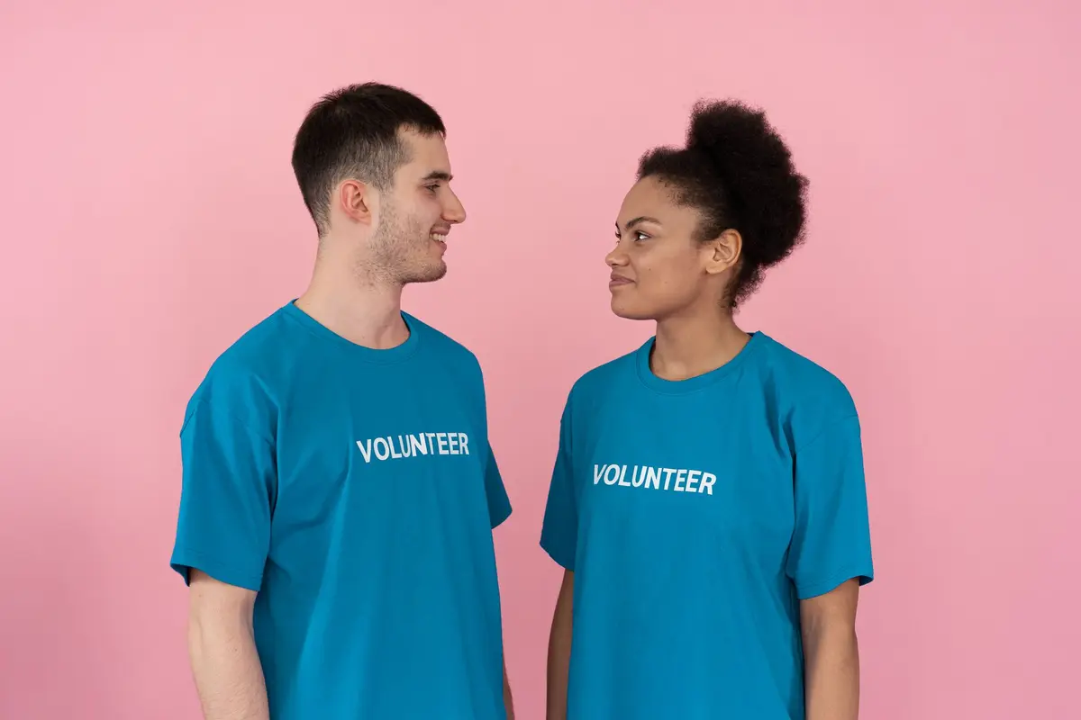 Two volunteers in matching teal shirts with VOLUNTEER printed on the chest