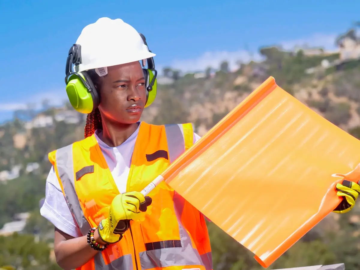 A flagger in a high-visibility safety vest and hard hat holding a traffic flag