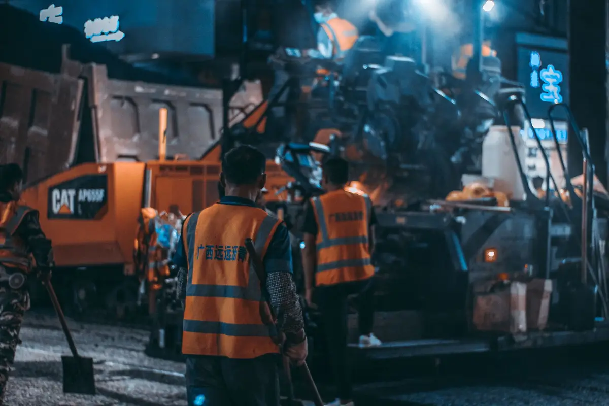 A road construction crew in high-visibility vests working with heavy machinery at night