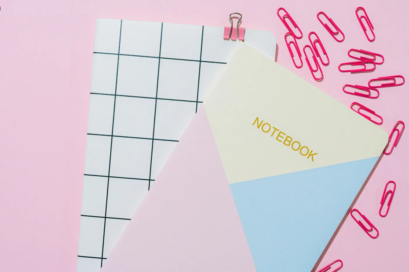 A flat lay of notebooks and stationery on a pink background