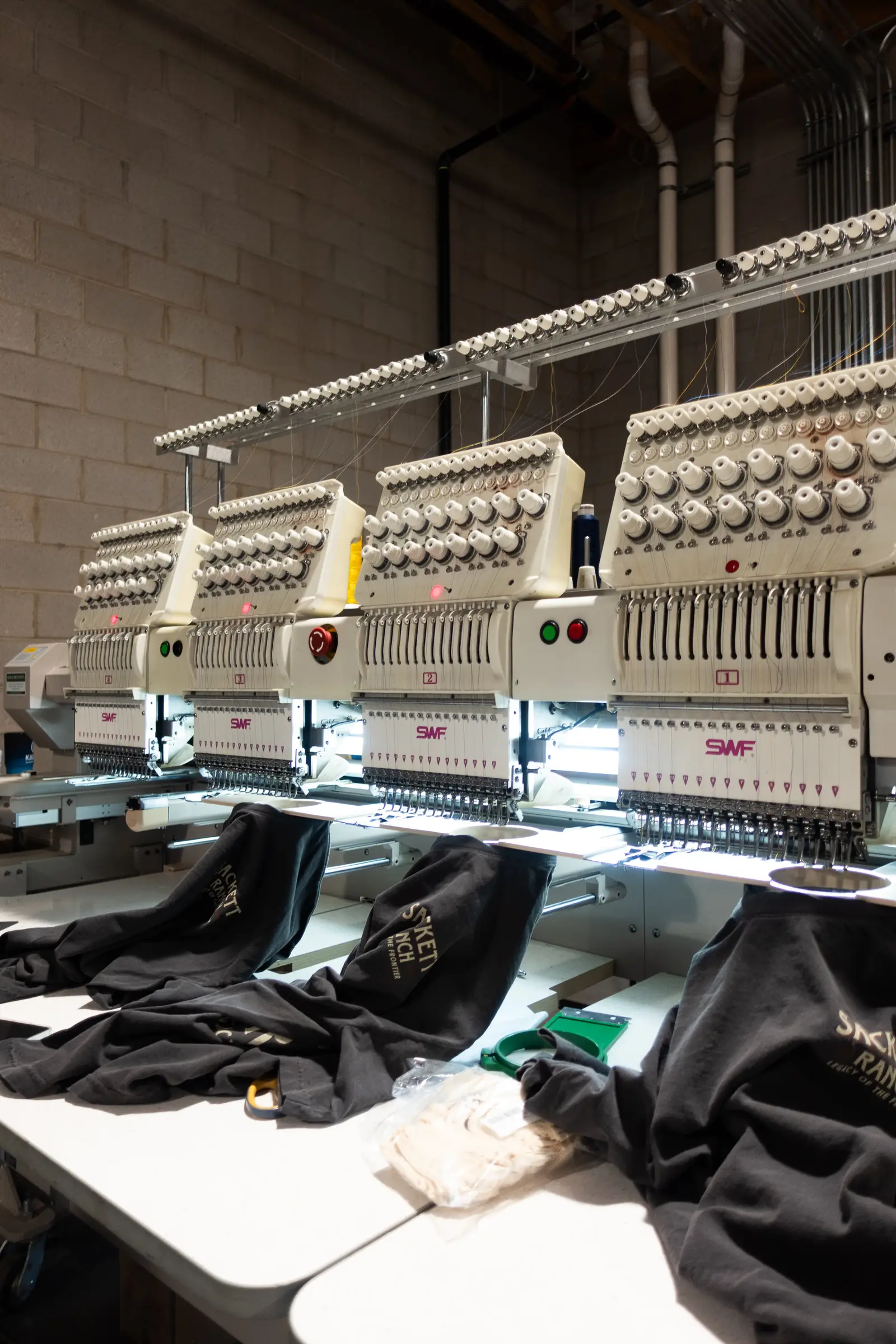 A row of commercial embroidery machines stitching gear in-house
