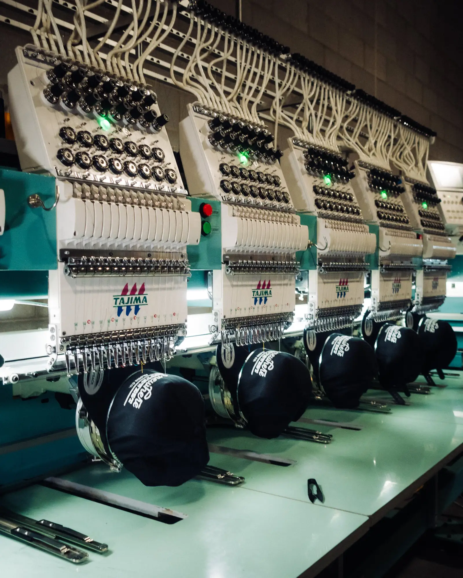A row of commercial Tajima embroidery machines stitching caps in the Heart & Hook shop