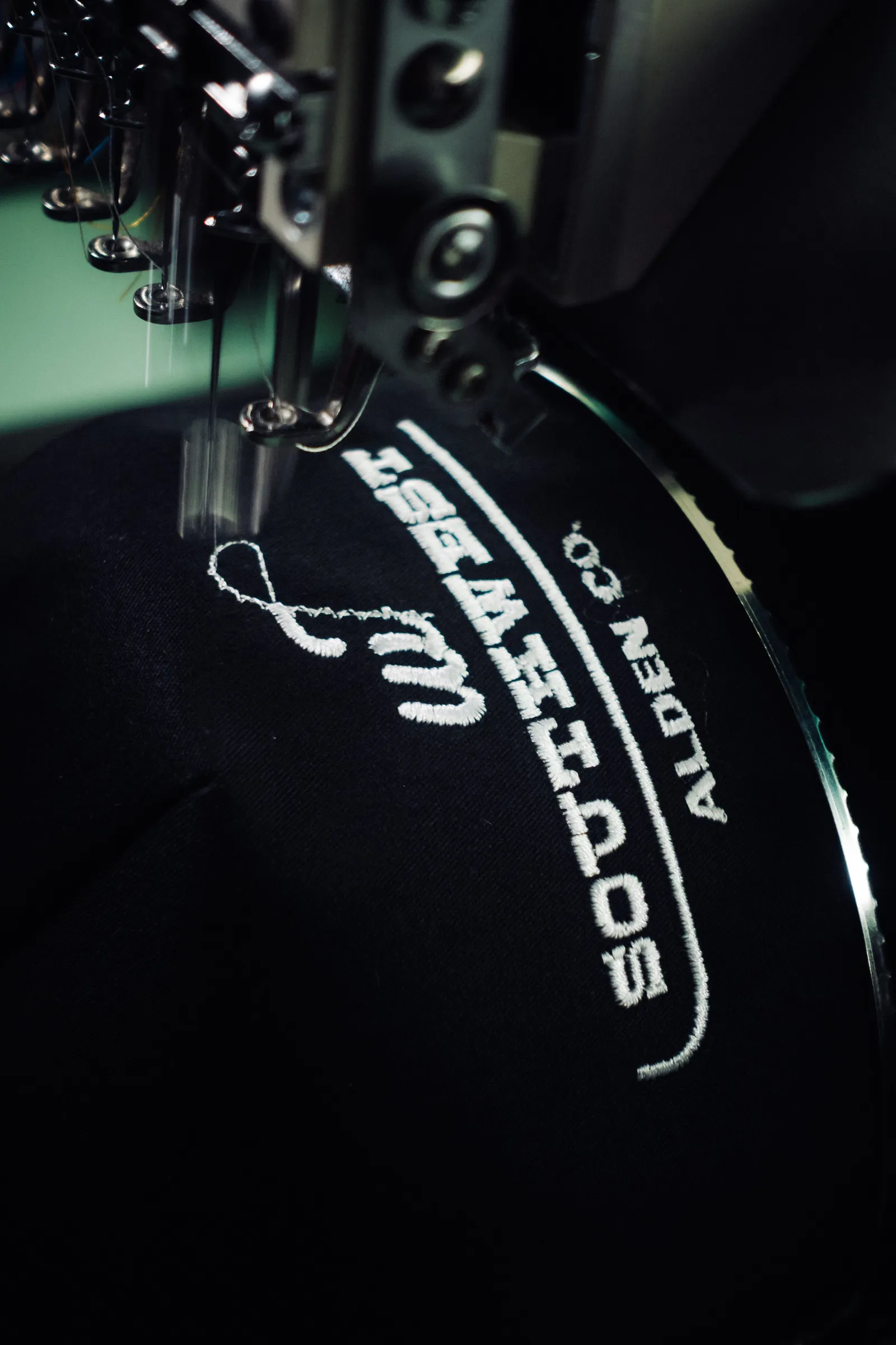 Close-up of a logo being embroidered onto a cap on a commercial machine