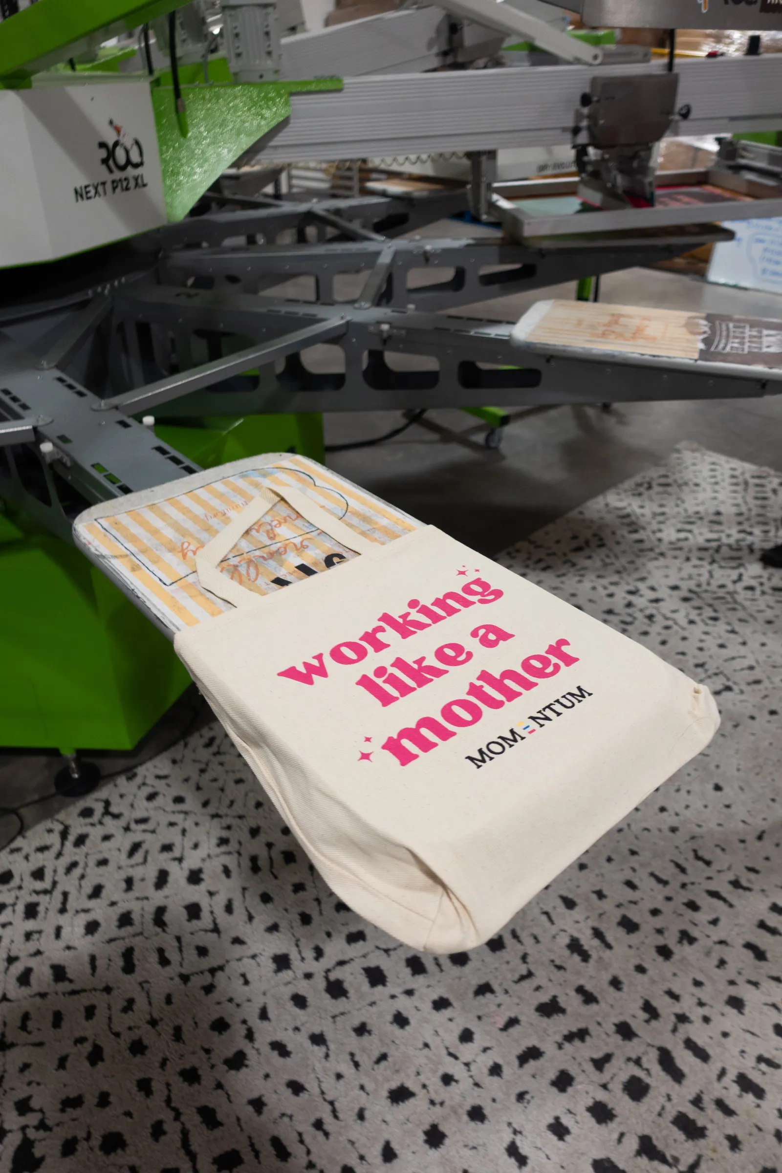 A custom screen-printed branded tote bag on the press